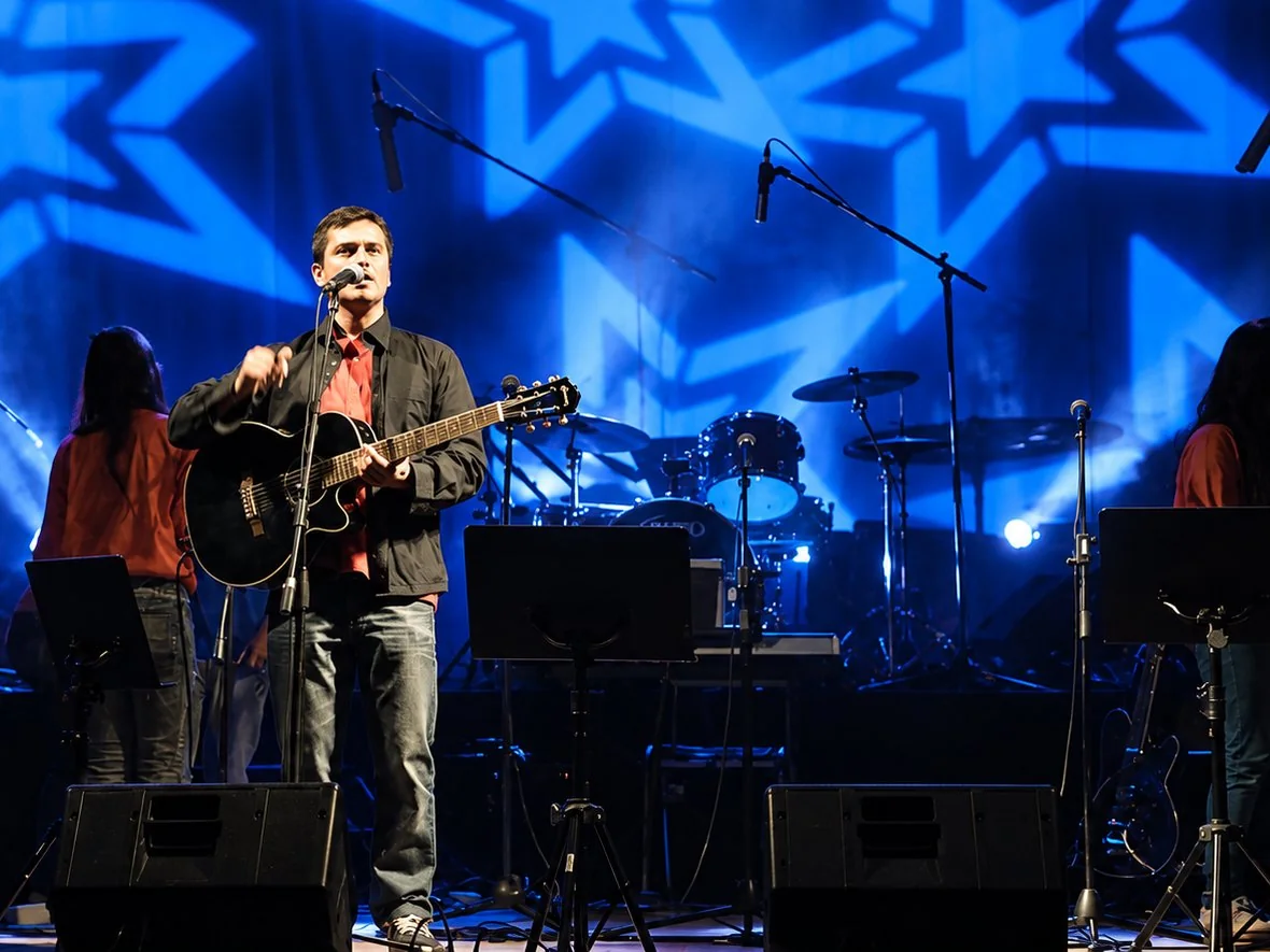 Alejandro Luna cantando con su guitarra en el escenario, con luces azules